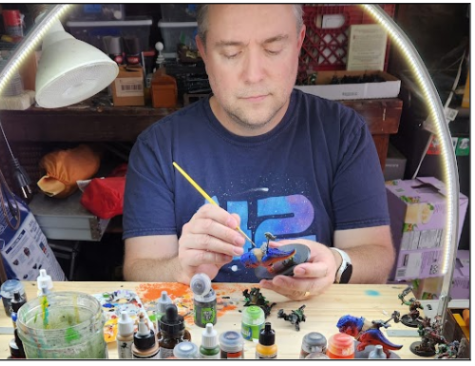 Warhammer club adviser Tarin Almstedt uses Nuln Oil paint to shade his Nob on Smasha Squig at his home painting studio. In the foreground is built but unpainted scenery for use in games of 40K.