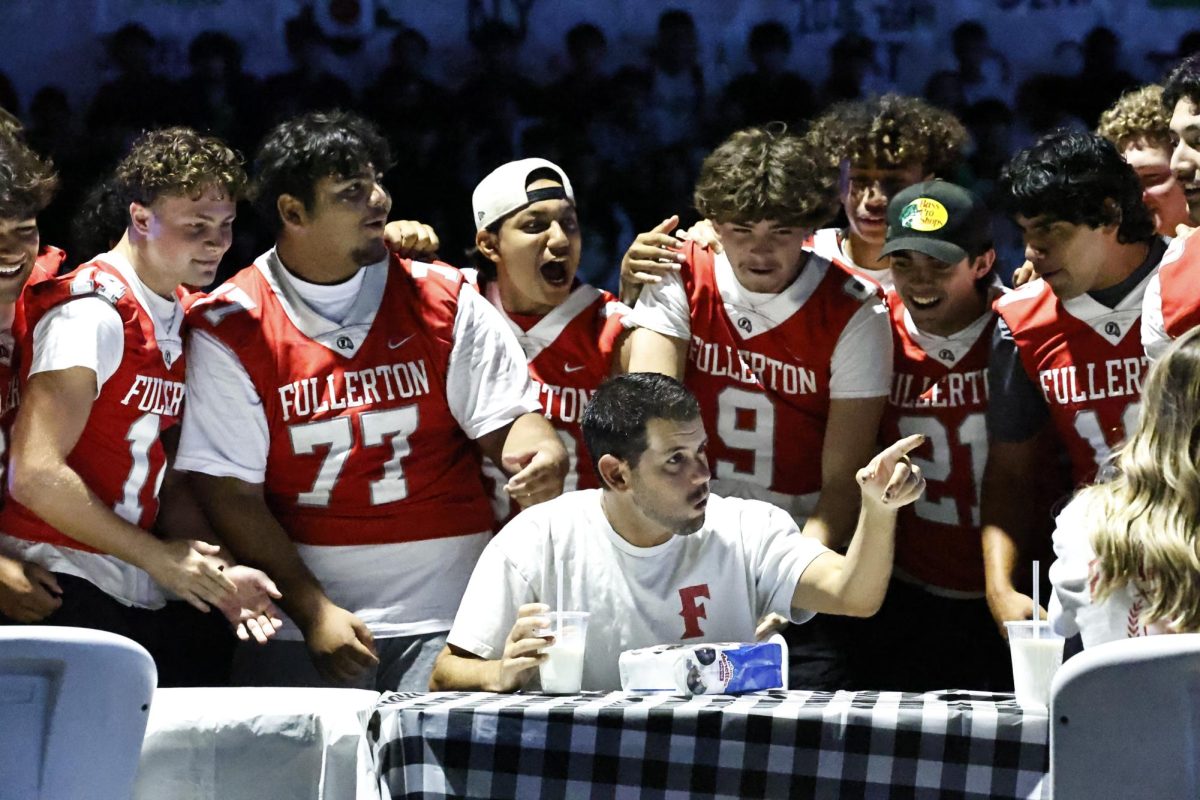 Head coach Pete Karavedas participated in the homecoming assembly donut eatingi contest on Sept. 19. He is supported by varsity football players cheering him on. Photo by Samantha Scopis for the Tribe Tribune